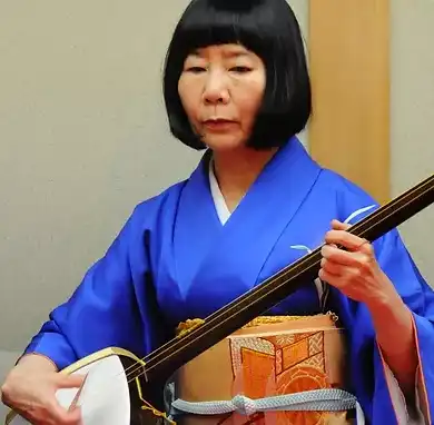 Makoto Nishimura in a deep blue kimono playing a shamisen